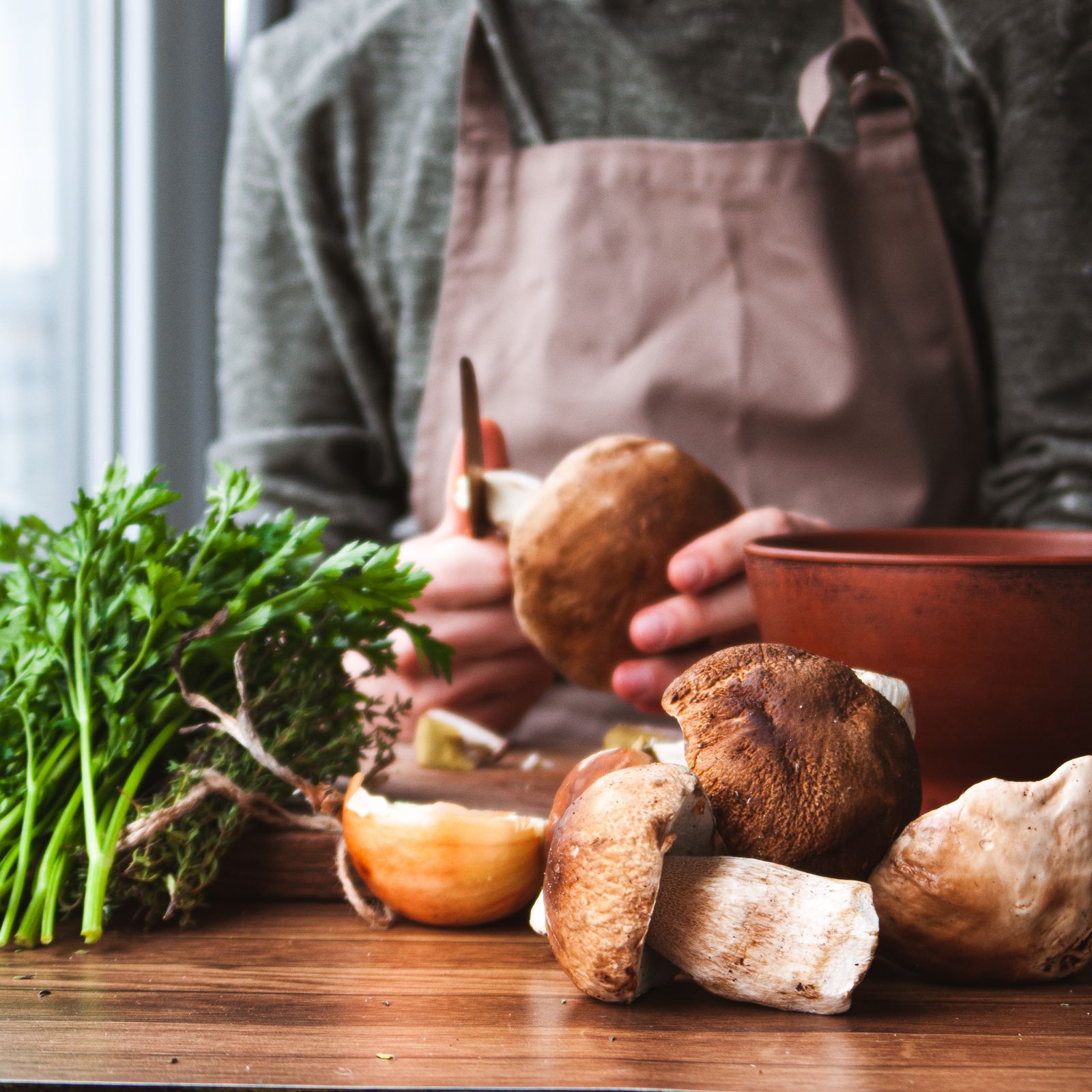 A cook preparing fresh mushrooms and herbs in a kitchen